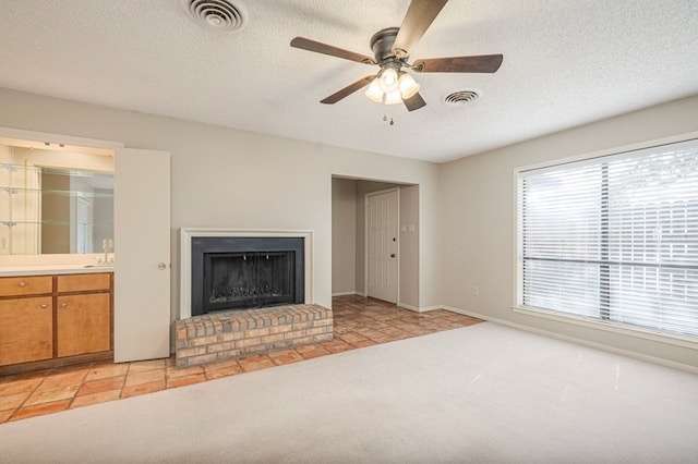 unfurnished living room with light carpet, a brick fireplace, visible vents, and a textured ceiling