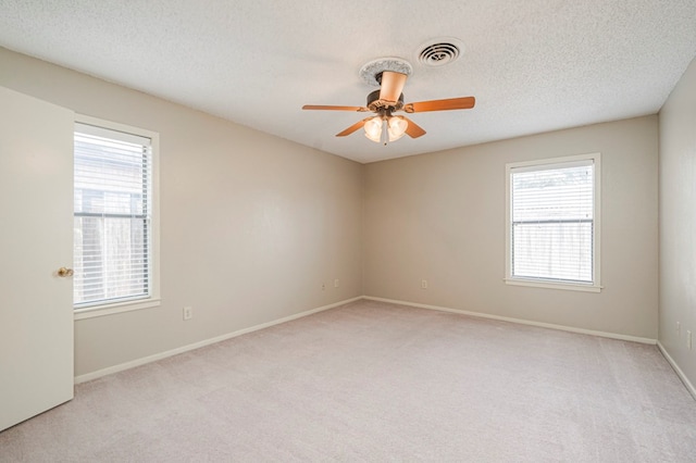 spare room with ceiling fan, visible vents, a textured ceiling, and light colored carpet