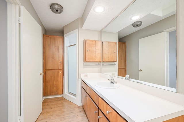 bathroom with a textured ceiling, wood finished floors, vanity, and a shower stall