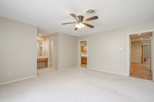 unfurnished bedroom featuring ensuite bathroom, a textured ceiling, visible vents, and light colored carpet