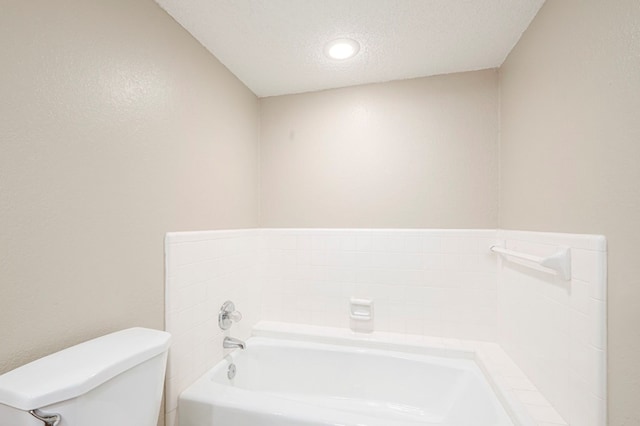 full bath featuring toilet, a garden tub, and a textured ceiling