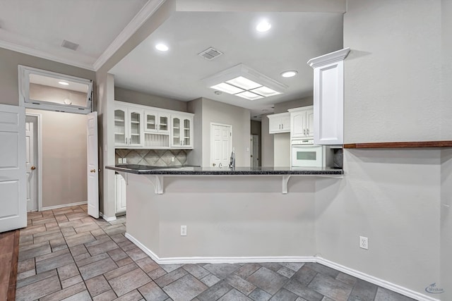 kitchen featuring a peninsula, white cabinets, white oven, dark countertops, and glass insert cabinets