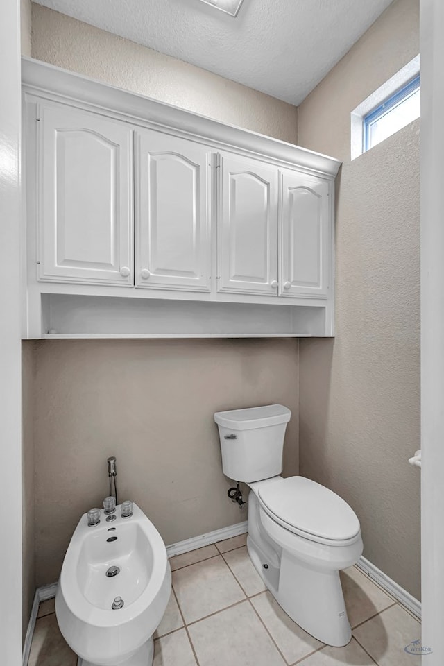 bathroom with a bidet, toilet, baseboards, and tile patterned floors