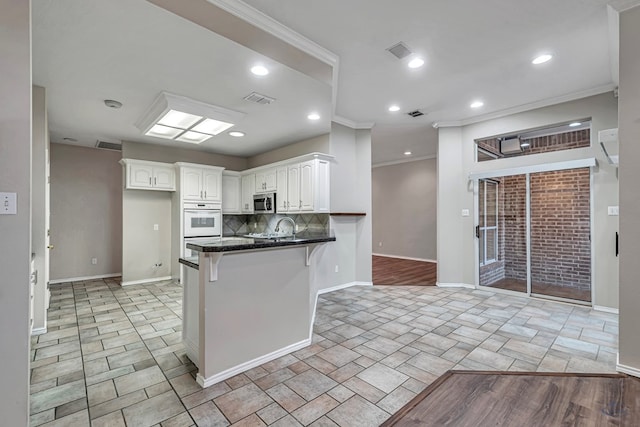 kitchen with a peninsula, visible vents, white cabinetry, tasteful backsplash, and stainless steel microwave