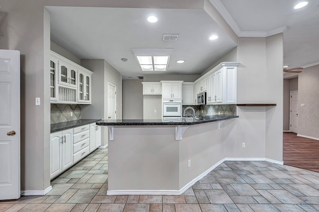 kitchen with visible vents, glass insert cabinets, white cabinetry, oven, and a peninsula