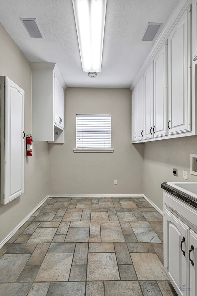 washroom featuring washer hookup, baseboards, cabinet space, stone finish flooring, and electric dryer hookup