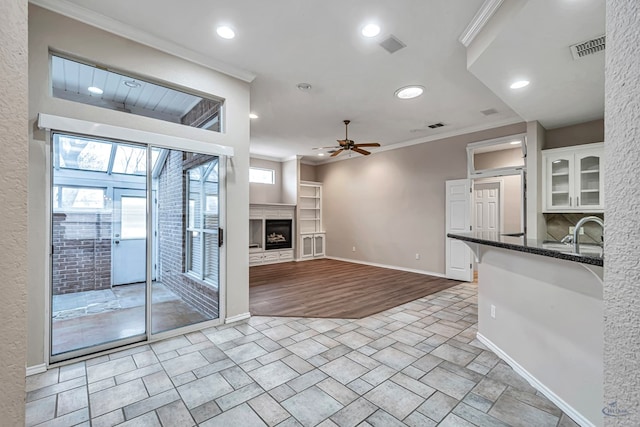 unfurnished living room featuring a fireplace, crown molding, visible vents, a ceiling fan, and baseboards