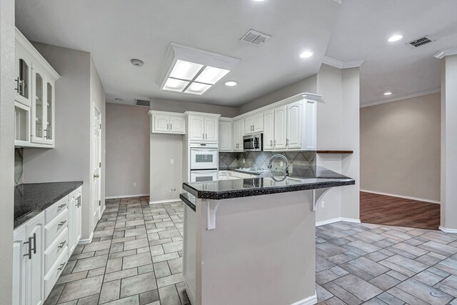 kitchen featuring visible vents, stainless steel microwave, white cabinets, a peninsula, and a kitchen bar