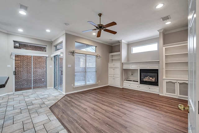 unfurnished living room with light wood-type flooring, a glass covered fireplace, visible vents, and crown molding