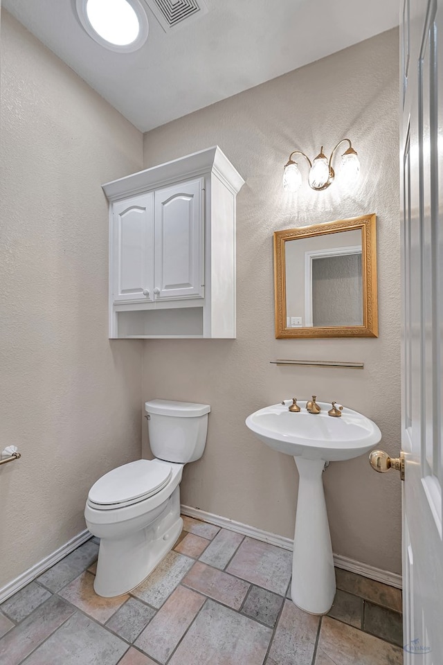 bathroom featuring toilet, baseboards, and stone tile floors