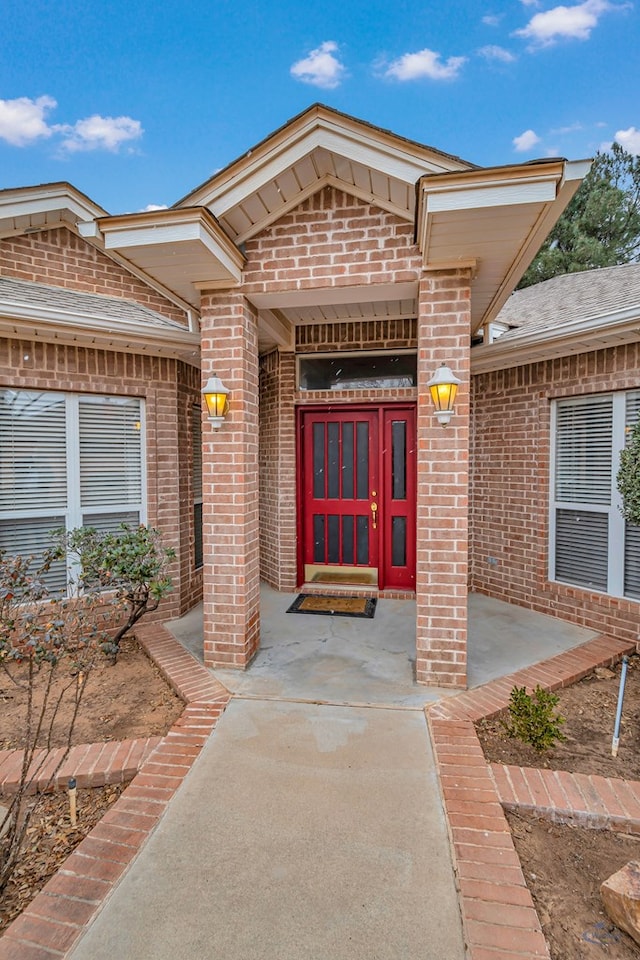 view of exterior entry with roof with shingles and brick siding