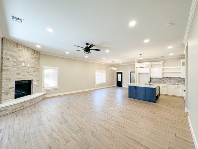 unfurnished living room featuring a fireplace, ceiling fan with notable chandelier, light hardwood / wood-style flooring, and ornamental molding