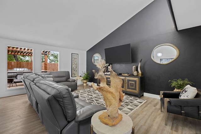 living room with light wood-type flooring, an accent wall, baseboards, and vaulted ceiling