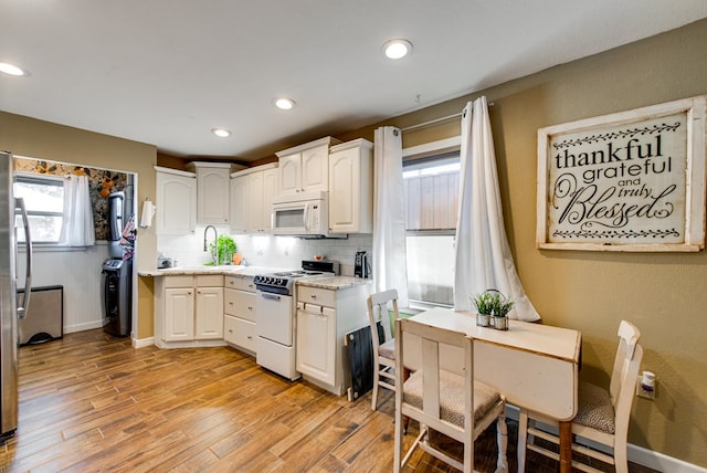 kitchen featuring backsplash, white appliances, washer / clothes dryer, light hardwood / wood-style floors, and white cabinetry