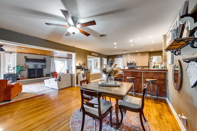 dining area with ceiling fan, light wood-type flooring, and a textured ceiling