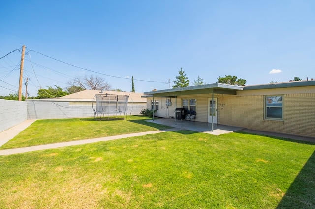 back of property with a lawn, a patio area, and a trampoline