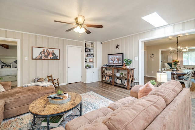 living room featuring ceiling fan with notable chandelier, a skylight, built in features, light wood-type flooring, and a textured ceiling