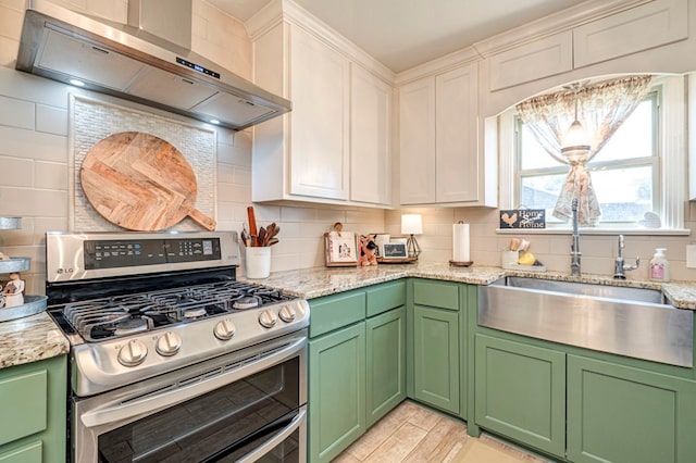 kitchen with wall chimney range hood, sink, gas stove, light stone counters, and white cabinetry