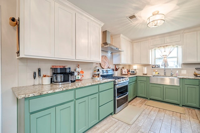 kitchen featuring sink, wall chimney range hood, light hardwood / wood-style flooring, range with two ovens, and white cabinets