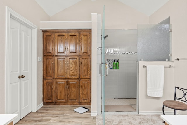 bathroom with wood-type flooring, a shower with shower door, and lofted ceiling