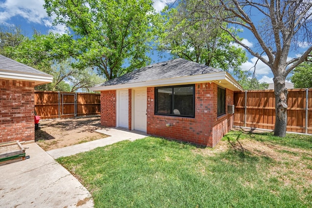 back of property featuring brick siding, a yard, an outbuilding, a fenced backyard, and a shingled roof