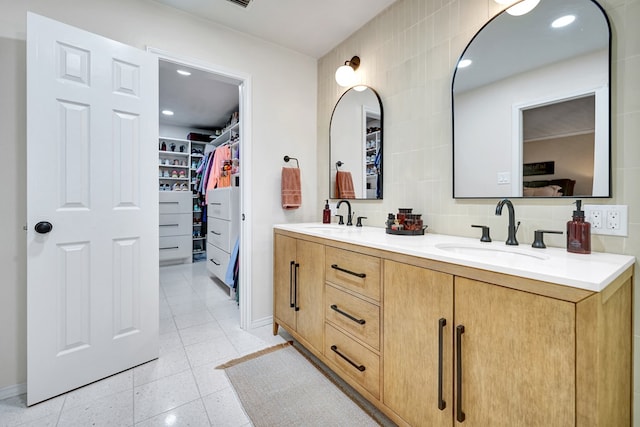 full bathroom with tile walls, a spacious closet, double vanity, and a sink