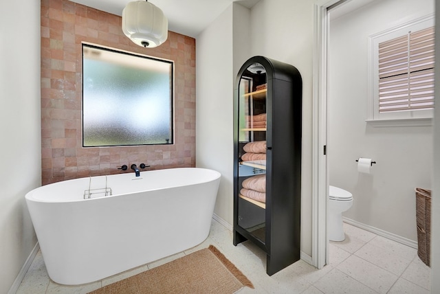 bathroom with a soaking tub, toilet, baseboards, and tile walls