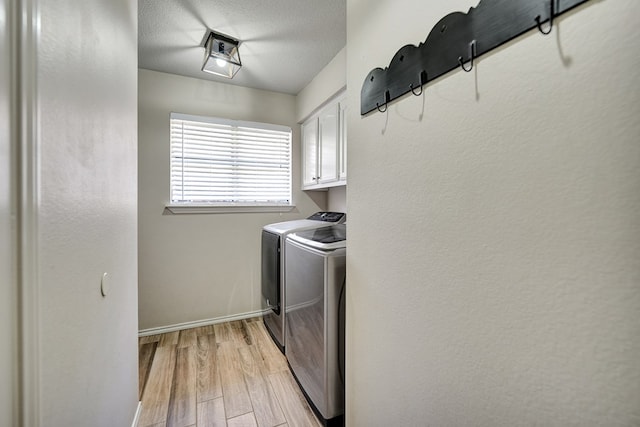 washroom featuring washing machine and dryer, a textured ceiling, baseboards, light wood-type flooring, and cabinet space
