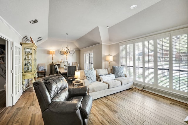 living area with lofted ceiling, an inviting chandelier, visible vents, and wood finished floors