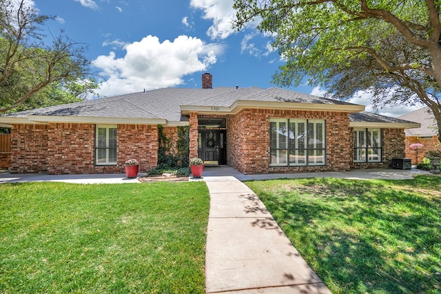 single story home featuring brick siding, a chimney, a front yard, and a patio