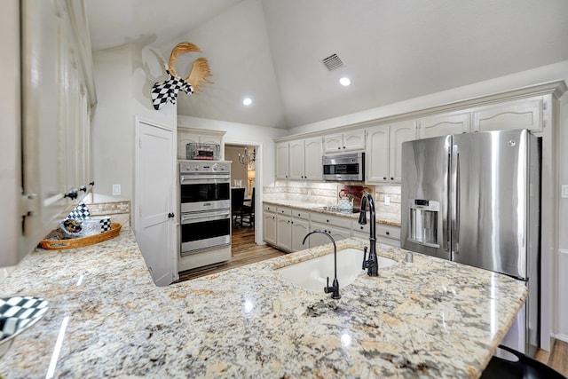 kitchen featuring visible vents, a sink, vaulted ceiling, backsplash, and appliances with stainless steel finishes