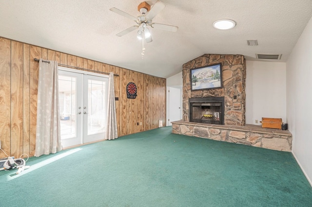 unfurnished living room featuring a stone fireplace, vaulted ceiling, a textured ceiling, wooden walls, and carpet floors