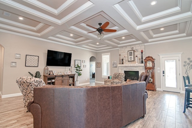 living area with a ceiling fan, light wood finished floors, coffered ceiling, a fireplace, and arched walkways