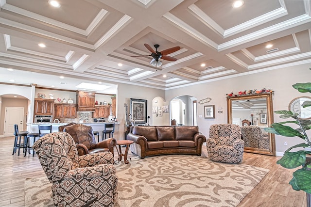 living room featuring arched walkways, light wood finished floors, coffered ceiling, and ceiling fan