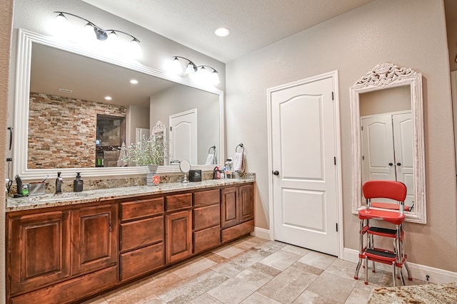 bathroom with double vanity, tiled shower, baseboards, and a sink