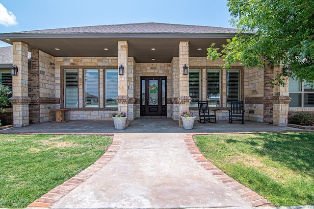 view of exterior entry with stone siding, covered porch, and a yard