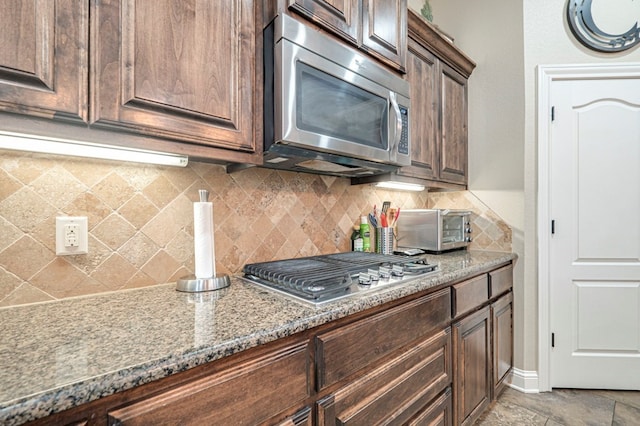 kitchen featuring backsplash, dark stone countertops, dark brown cabinetry, and stainless steel appliances