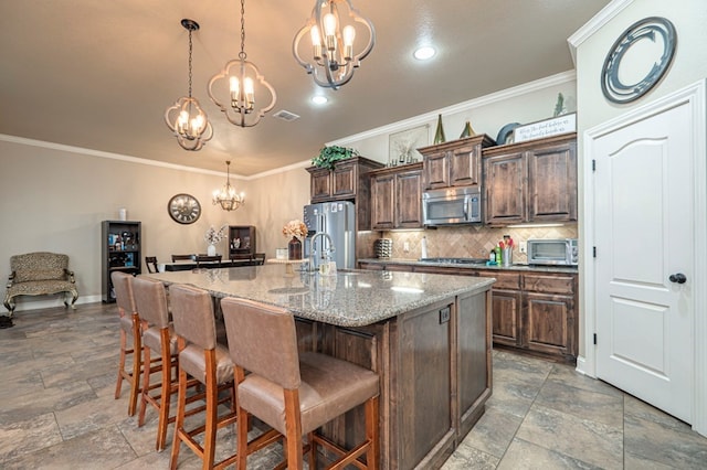 kitchen featuring a kitchen island with sink, a kitchen breakfast bar, decorative light fixtures, light stone counters, and stainless steel appliances