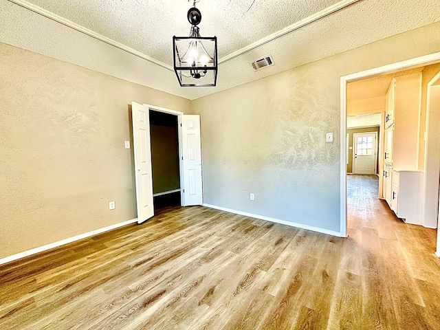 spare room featuring a notable chandelier, a textured ceiling, and light wood-type flooring