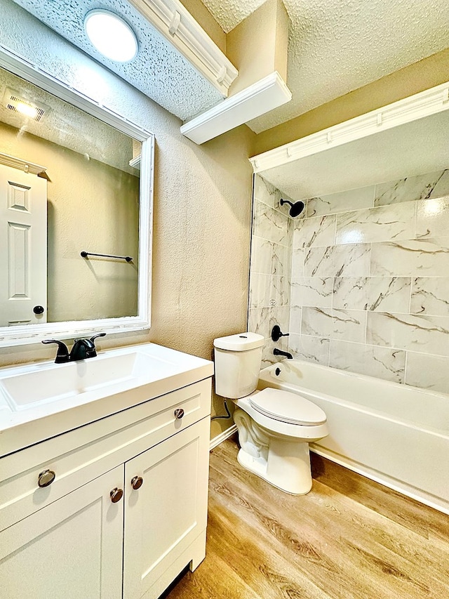 full bathroom with tiled shower / bath, hardwood / wood-style flooring, vanity, toilet, and a textured ceiling