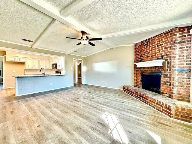 unfurnished living room with a fireplace, lofted ceiling with beams, a textured ceiling, and light wood-type flooring