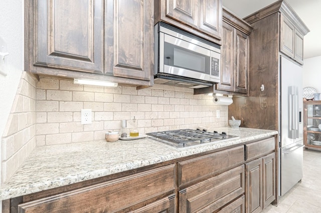 kitchen with stainless steel appliances, dark brown cabinetry, light stone counters, and decorative backsplash