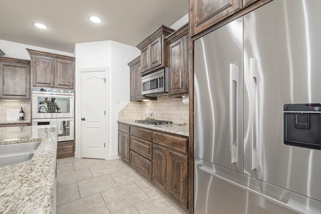 kitchen with light stone counters, decorative backsplash, appliances with stainless steel finishes, light tile patterned flooring, and dark brown cabinetry