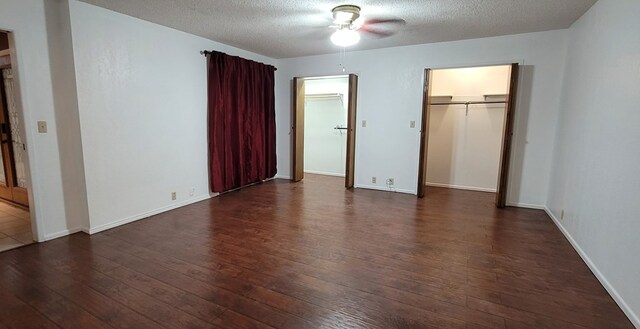 unfurnished bedroom with a walk in closet, a textured ceiling, ceiling fan, dark wood-type flooring, and a closet