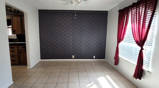 tiled empty room featuring a textured ceiling, ceiling fan, and a healthy amount of sunlight