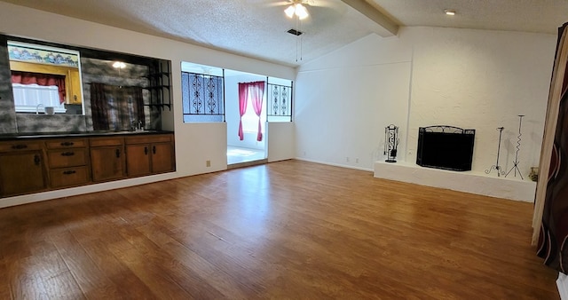 unfurnished living room featuring hardwood / wood-style flooring, lofted ceiling with beams, and a textured ceiling