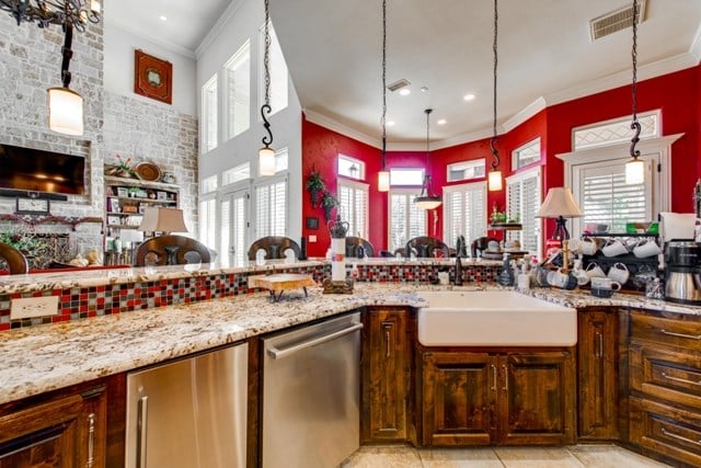 kitchen with light tile patterned floors, stainless steel appliances, hanging light fixtures, light stone counters, and sink