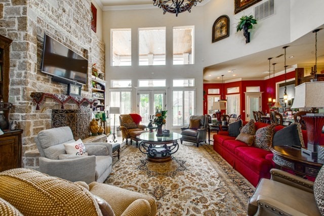 living room with crown molding, a towering ceiling, a stone fireplace, and a chandelier