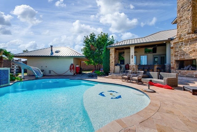 view of swimming pool with a patio area, an outdoor stone fireplace, a water slide, and ceiling fan