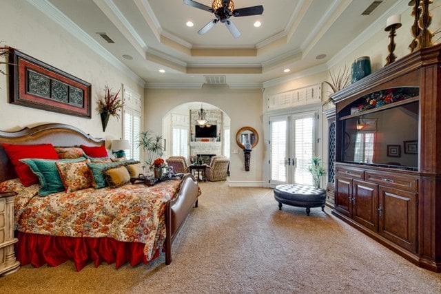 bedroom with ornamental molding, light colored carpet, a tray ceiling, and multiple windows